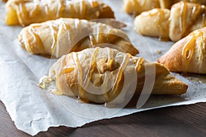 Close up of a parchment lined baking tray of freshly baked apple crescent rolls topped with caramel sauce.
