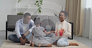 Close-up parents afro american couple sitting together on living room floor listening to little cute daughter of child