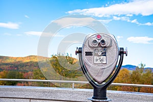 Close up of park binoculars with wooded mountains at the peak of fall foliage in background