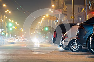 Close up of parked cars on roadside at night with blurred view of traffic lights of moving vehicles on city street