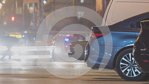 Close up of parked cars on roadside at night with blurred view of traffic lights of moving vehicles on city street