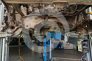 Close-up on the part of the car bottom from the front of the exhaust pipe, engine disassembled on blue crane during the repair in