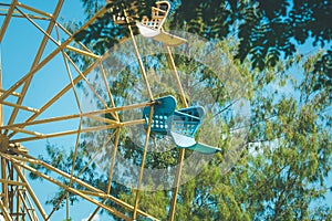 Close up part of colorful ferris wheel with green tree and blue sky background.