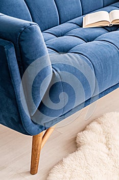 Close-up of a part a couch dressed in luxurious navy blue tapestry in a living room interior. An open book on the sofa. Real photo