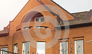 Close-up of a part of the facade of a red brick cottage house with windows and a roof, modern urban construction