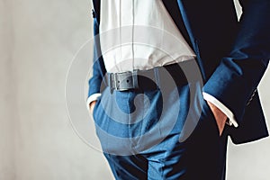Close up part of man body in blue suit with hands in pockets on white background
