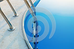 Close-up of a part of swimming pool with a stainless steel ladder and blue water on sunset. Summer vacation, holidays, relax