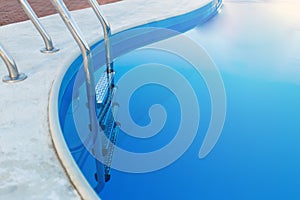 Close-up of a part of swimming pool with a stainless steel ladder and blue water on sunset. Summer vacation, holidays,