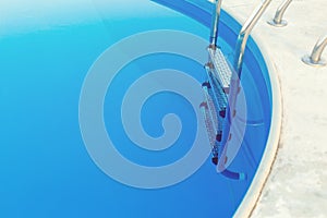 Close-up of a part of swimming pool with a stainless steel ladder and blue water on sunset. Summer vacation, holidays, relax