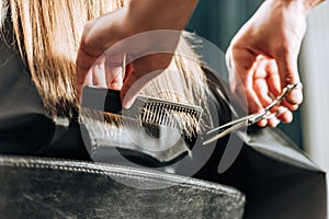 Close-up partial view of hairstylist cutting hair to beautiful young woman