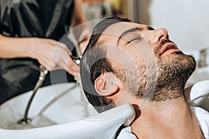 Close-up partial view of hairstylist washing hair to handsome young male client