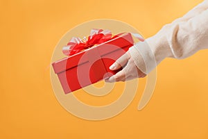 Close-up partial view of man in sweater holding red gift box on yellow background.Gift giving concept