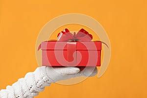 Close-up partial view of man in sweater holding red gift box on yellow background.Gift giving concept