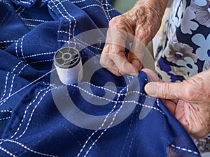 Close-up partial view of old woman hands using needle and thread to mend cloth