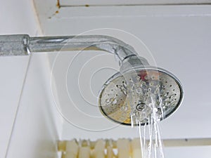 Close up of a partly clogged shower head in a bathroom, causing it to putting out so little water