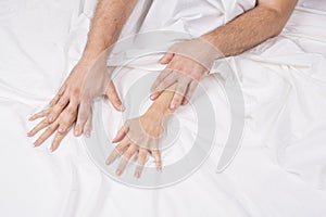 Close up of passionate couple hold hands during making intense love in bedroom, lovers enjoy hot sex on white sheet