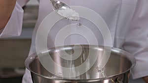 Close-up of a pastry chef spooning powdered sugar into a bowl of buttercream.