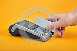 Close-up of payment machine buttons with human hand holding plastic card near by on yellow background