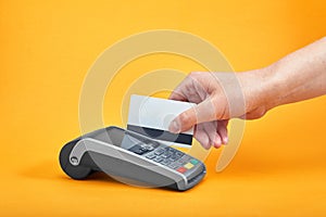 Close-up of payment machine buttons with human hand holding plastic card near by on yellow background