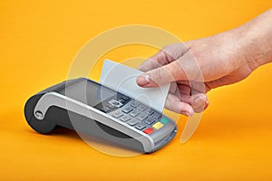 Close-up of payment machine buttons with human hand holding plastic card near by on yellow background