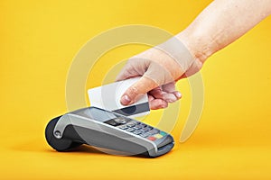 Close-up of payment machine buttons with human hand holding plastic card near by on yellow background