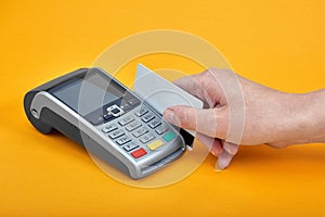 Close-up of payment machine buttons with human hand holding plastic card near by on yellow background