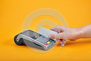 Close-up of payment machine buttons with human hand holding plastic card near by on yellow background