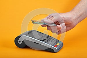 Close-up of payment machine buttons with human hand holding plastic card near by on yellow background