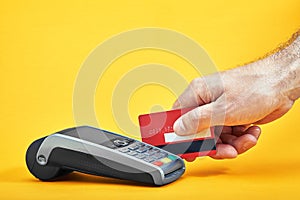 Close-up of payment machine buttons with human hand holding plastic card near by on yellow background