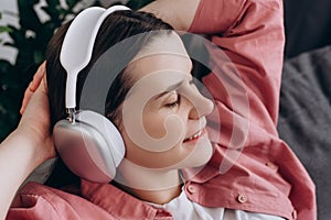 Close up of peaceful happy relaxed young woman wearing headphones listening to music, leaning back on couch at home, mindful calm