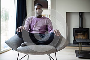 Close Up Of Peaceful Teenage Boy Meditating Sitting In Chair At Home