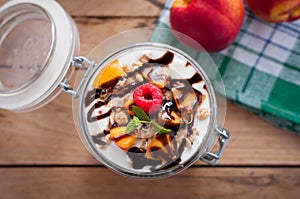 Close-up of peach parfait with yogurt, granola and chocolate topping in a jar, top view