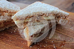 Close-up of Peanut butter banana sandwiches on wooden background. Slices of whole wheat bran bread with peanut paste on cutboard