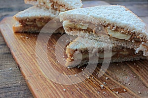 Close-up of Peanut butter banana sandwiches on wooden background. Slices of whole wheat bran bread with peanut paste on cutboard