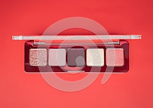 A close-up of pearlescent shimmery palette of pink eyeshadows for creating eye makeup on red background.