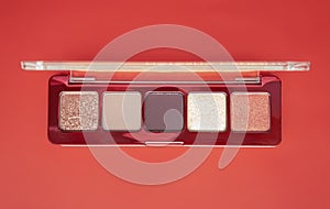 A close-up of pearlescent shimmery palette of pink eyeshadows for creating eye makeup on red background.