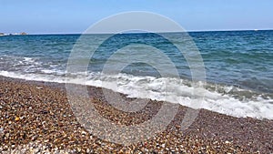 Close-up of pebble beach with transparent waves with sun glare on the water. Close up of stony sea shore. Natual