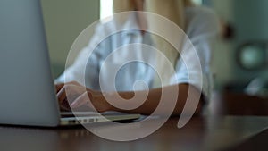 Close-up pedestal shot of attractive young business woman typing on laptop keyboard, sitting at desk in cafe.