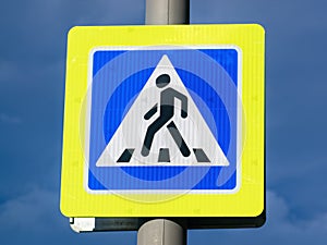 Close-up pedestrian crossing sign with bright yellow frame on cloudy dark blue sky background