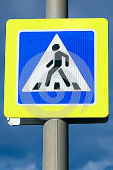 Close-up pedestrian crossing sign with bright yellow frame on cloudy dark blue sky background