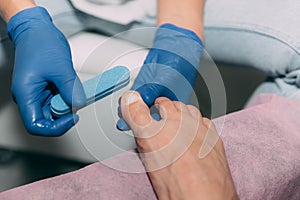 Close-up pedicure process in salon. Foot care treatment and nail. Sanding nails with a nail file. Master in blue gloves makes pedi