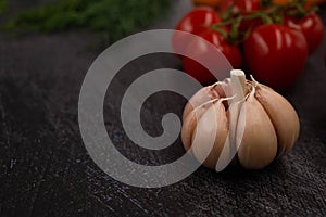 Close-up of a peeled head of garlic on a black metal background with cherry tomatoes in the background. Copy space