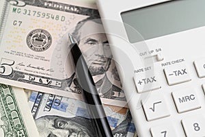 Close up of pen and calculator with tax plus and tax minus buttons on US Dollar banknotes money using as financial activities