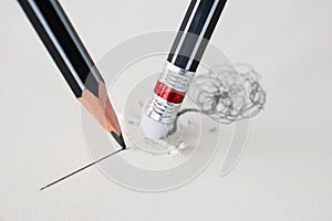 Close up of a pencil eraser removing a crooked line and the close up of a sharpened pencil writing a straight line.