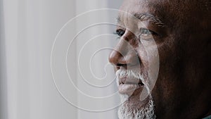 Close up pensive male old wrinkled face, 60s African bearded man deep in sad thoughts looking at window, elderly