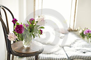 Close up of peonies in a vase on a vintage wooden chair. Rustic style interior with mattresses, pillows and flowers near an open