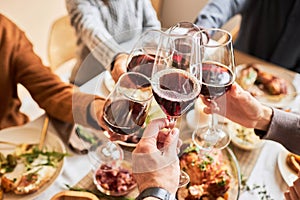 Close up of people toasting with red wine glasses at festive dinner table