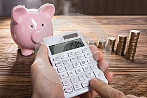 Person Calculating On Calculator With Piggybank And Coin Stacked