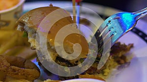 Close-up of person cutting burger piece, fatty and high-calorie food, obesity