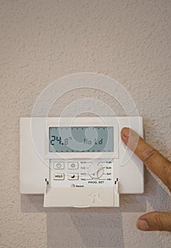 Close-up Of person hand setting Temperature On Digital Thermostat at home attached To Wall. Copy space